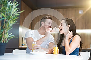 Young lovely couple eating croissant and drinkink orange juice for breakfast in the kitchen man feeds his wife start of