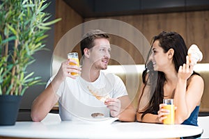 Young lovely couple eating croissant and drinkink orange juice for breakfast in the kitchen start of great day