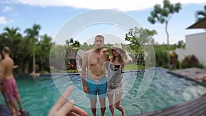 Young lovely couple photographed and fall into swimming pool at tropical vacation villa.