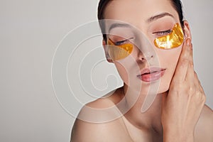 Young lovely girl applying golden collagen patches under her eyes