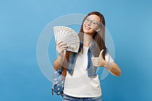 Young lovely happy woman student in glasses with backpack showing thumb up holding bundle lots of dollars, cash money