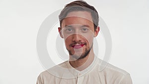 Young lover handsome brunette guy with brown beard, painted lips by women red lipstick wear shirt, look at camera, blow kiss