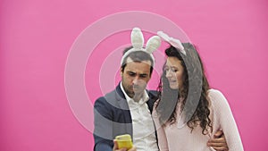 Young lovers couple on the pink background. With hackneyed ears on the head. During this, the girl wears rabbit ears to