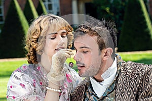 Young lovers dressed in vintage clothing. Man looks on as his partner feeds him a cherry