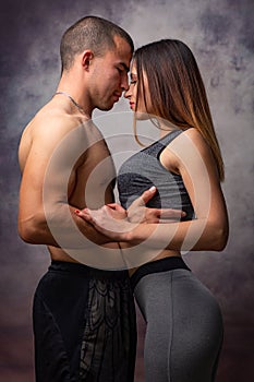 Young loving couple of athletic physique cuddles on grey background