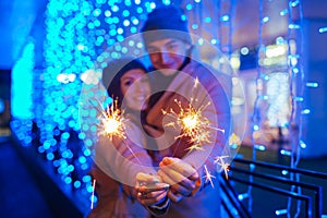 Young loving couple burning sparklers by holiday illumination