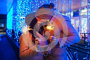 Young loving couple burning sparklers by holiday illumination