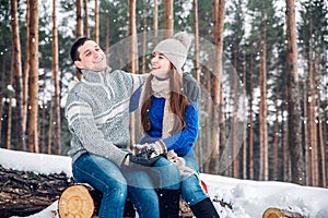 Young loving couple dressed in blue sweater sitting on the firewood and hugging in winter forest