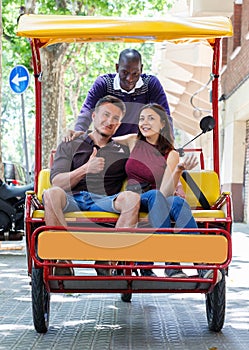 Young loving couple enjoying tour of city on trishaw with affable African American driver