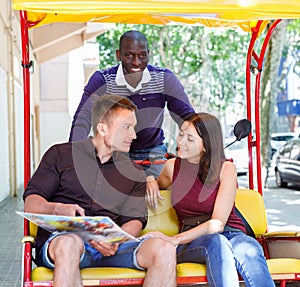 Young loving couple enjoying tour of city on trishaw with affable African American driver