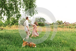 Young loving couple having fun and running on the green grass on the lawn with their beloved domestic dog breed Beagle and a