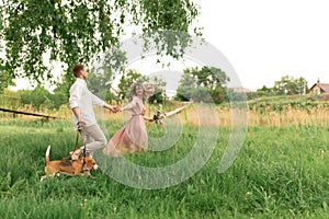 Young loving couple having fun and running on the green grass on the lawn with their beloved domestic dog breed Beagle and a