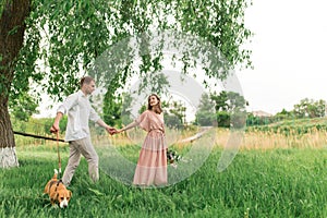 Young loving couple having fun and running on the green grass on the lawn with their beloved domestic dog breed Beagle and a