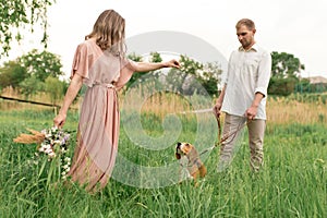 Young loving couple having fun and running on the green grass on the lawn with their beloved domestic dog breed Beagle and a