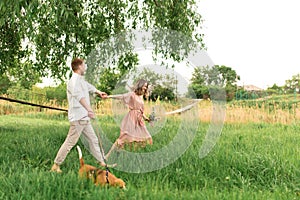 Young loving couple having fun and running on the green grass on the lawn with their beloved domestic dog breed Beagle and a
