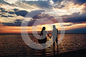 Young loving couple holding hands at sunset on the lake