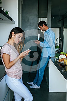 Young loving couple at the kitchen have a breakfast using mobile phones