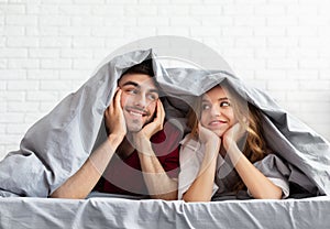 Young loving couple lying in bed under blanket