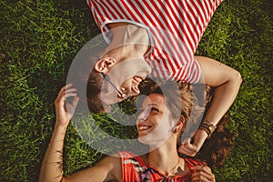 Young loving couple lying together head to head on a grass at summer. Both in red clothes and holding hands. Overhead top view