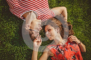 Young loving couple lying together head to head on a grass at summer. Family picnic. Both in red clothes and holding hands. Overhe