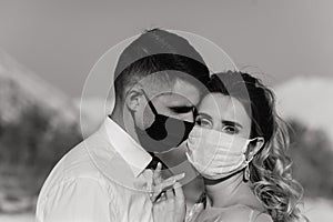 Young loving couple in medical masks in park during quarantine on wedding day