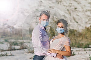 Young loving couple in medical masks in park during quarantine on wedding day.