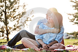 Young loving couple outdoors sitting on grass, hugging and looking away.