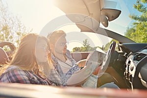 Young loving couple planning their romantic adventure. Joyful young couple smiling while riding in their convertible