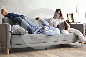 Young loving couple relaxing on sofa together, husband lying on wife legs resting on couch photo