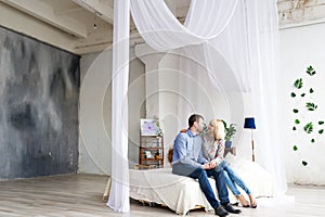 Young loving couple sitting on the bed, kissing and hugging.