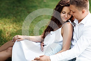 Young loving couple is sitting on grass in the park, hugging, fooling around and enjoying nature