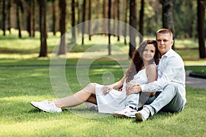 young loving couple is sitting on grass in the park, hugging, fooling around and enjoying nature