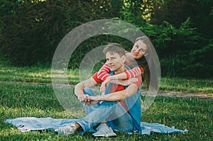 Young loving couple is sitting on a plaid in the park, hugging, fooling around and enjoying nature. Picnic for couples in love