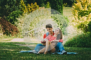 Young loving couple is sitting on a plaid in the park, hugging, fooling around and enjoying nature. Picnic for couples in love