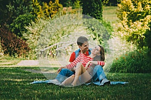 Young loving couple is sitting on a plaid in the park, hugging, fooling around and enjoying nature. Picnic for couples in love