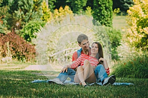 Young loving couple is sitting on a plaid in the park, hugging, fooling around and enjoying nature. Picnic for couples in love