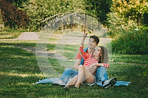 Young loving couple is sitting on a plaid in the park, hugging, fooling around and enjoying nature. Picnic for couples in love