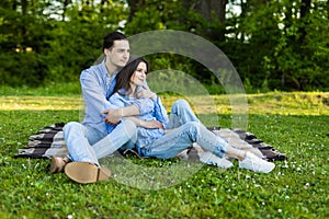 Young loving couple is sitting on a plaid in the park, hugging, fooling around and enjoying nature. Picnic for couples in love.