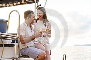 Young loving couple sitting on the yacht deck and drinking wine