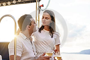 Young loving couple sitting on the yacht deck and drinking wine