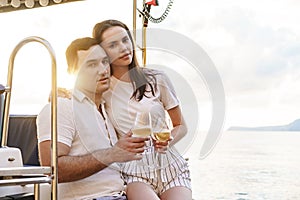 Young loving couple sitting on the yacht deck and drinking wine