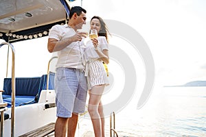 Young loving couple sitting on the yacht deck and drinking wine