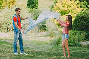 Young loving couple spreads a plaid on a meadow in the park. Picnic for couples in love