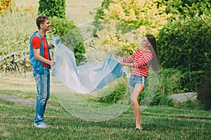 Young loving couple spreads a plaid on a meadow in the park. Picnic for couples in love