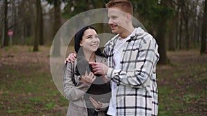 Young loving couple standing with puppy in park smiling. Medium shot portrait of Caucasian man and woman enjoying