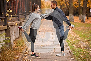 Young couple stretching leg muscles standing in a park and looking at each other.