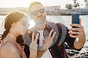 Young loving couple on vacation at the beach takes a funny selfie with smartphone - Boyfriend and girlfriend share their moments