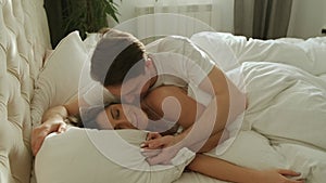 Young loving couple wake up in the morning. Man kiss and hug his wife in the bed.
