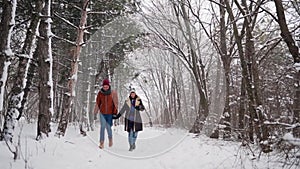 Young loving couple walking in a park on snowfall. Man holds his girlfriend`s hand on winter day. Woman stroll in snowy