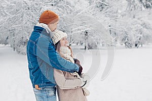 Young loving couple walking in winter park. Man and woman hugging enjoying snowy landscape outdoors